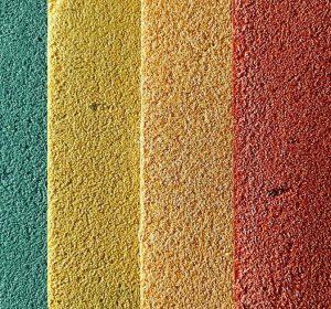 Colorful textured plaster wall finish samples in blue, green, yellow, orange, red, and white, arranged vertically on a neutral background